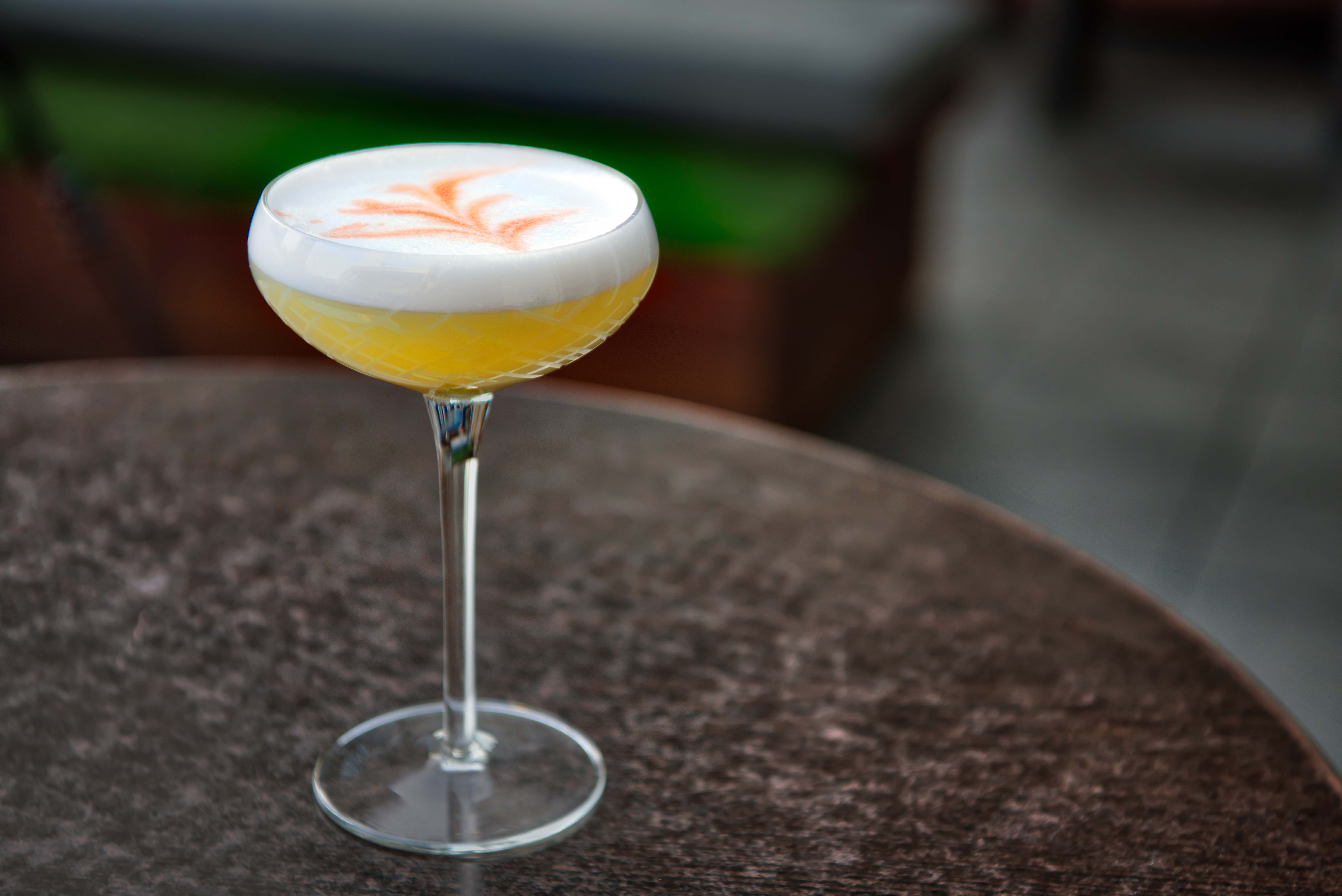 Vibrant yellow cocktail with decorative foam in long-stemmed coupe glass